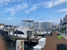 Marina with several fishing boats docked along a wooden pier under a bright blue sky with scattered clouds.