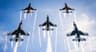 Five fighter jets in a tight formation with smoke trails against a clear blue sky across an air show.